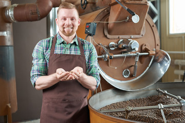 Waist up portrait of handsome young man wearing apron standing by coffee roasting machine holding...