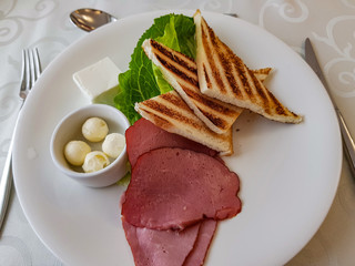 Toasts, ham, cold-boiled pork, lettuce, butter and cheese on a white plate
