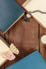 Overhead photo of books on dark background with vintage watch, paper butterfly, and copy space