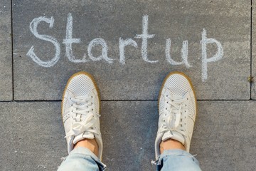View from above, female feet with text startup written on grey sidewalk