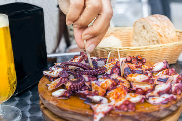People eating Pulpo a la Gallega Wooden plate. Galician style cooked octopus with paprika and olive oil.