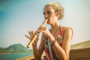 Young woman sitting on boat and playing bamboo flute © guruXOX