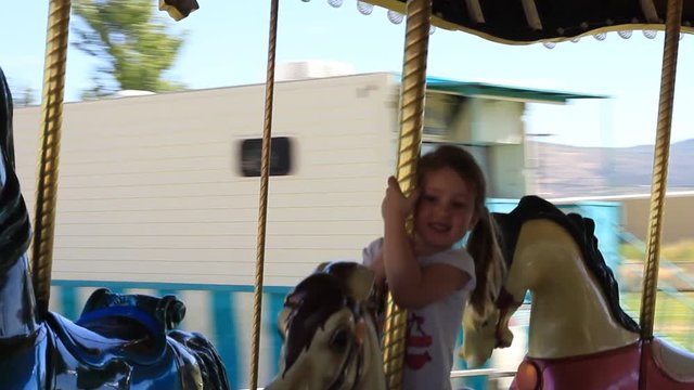 A little girl goes around and around and up and down on a fake pony attached to the carousel