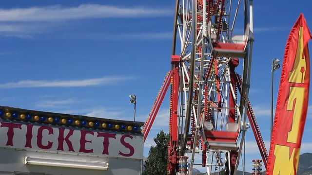 Panning shot of ticket booth at the carnival, and a spinning Ferris Wheel.