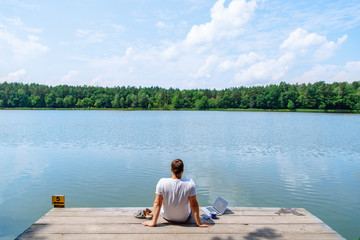 man sitting with laptop and looking on lake. working at vacation. summer time concept