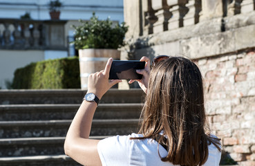 The girl photographs a mobile phone in the castle garden