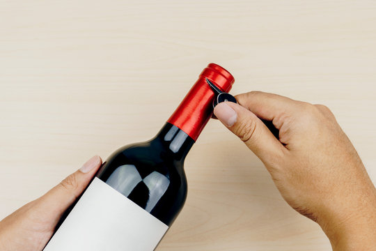 hand using a metal corkscrew knife to cut the foil capsule of the red wine bottle