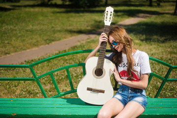 Beautiful young hipster girl posing with guitar outdoors in the Park