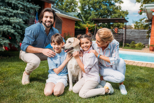 happy family with labrador dog looking at camera while spending time on backyard of country house on summer day
