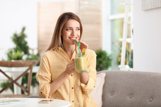 Young woman with tasty healthy smoothie at table, indoors
