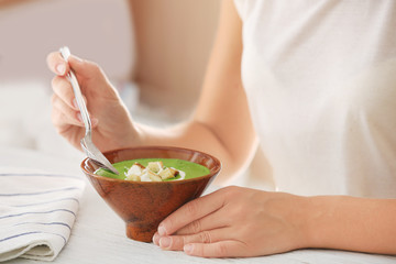 Woman eating tasty spinach soup in kitchen