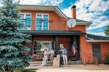 Fototapeta premium family with cardboard boxes and labrador dog standing on country house porch, moving home concept