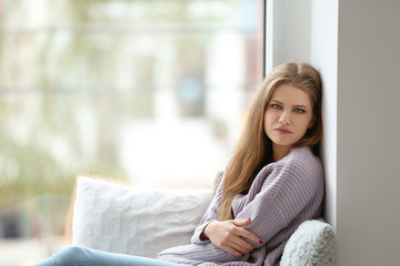 Obraz premium Young sad woman sitting near window at home