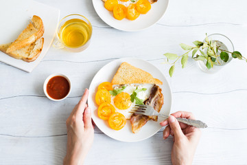 Woman's hands as she eats healthy breakfast.Eggs and bacon with yellow tomatoes on the wooden table.Top view