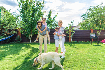 cheerful family with labrador dog spending time together on backyard on summer day