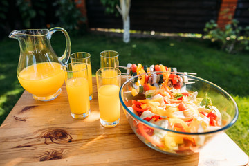 close up view of glasses of juice and salad with fresh vegetables on wooden surface on backyard