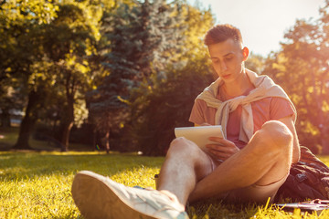 Handsome college man writing notes in copybook in campus park. Happy guy student learning outdoors...