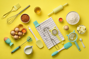 Healthy baking ingredients - butter, sugar, flour, eggs, oil, spoon, rolling pin, brush, whisk, towel over yellow background. Bakery food frame, cooking concept. Top view, copy space. Flat lay
