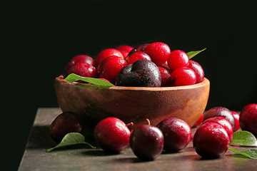 Bowl with ripe juicy plums on dark background