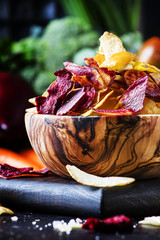 Vegan snacks, multicolored vegetable chips in  wooden bowl, background from  set of fresh farmer...