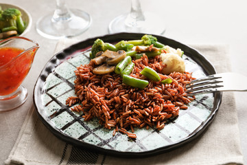 Plate with delicious brown rice and vegetables on table