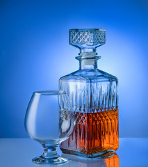 Glass of brandy with ice and a square decanter isolated on a blue background