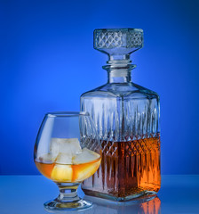 Glass of brandy with ice and a square decanter isolated on a blue background