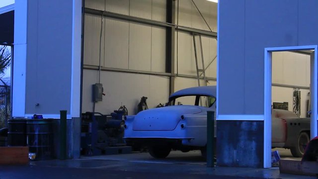 Antique car pulling out of the body shop in primer, with a new fender.
