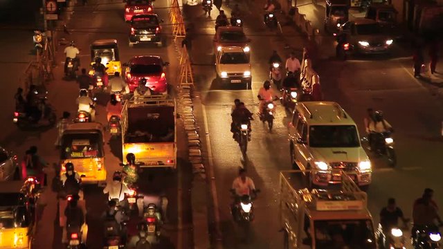 Rush hour in India, crowded traffic with cars, motorbikes, buses and many people. High angle, long shot.