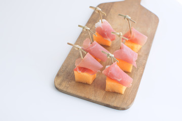 Melon with prociutto canapes on skewers Melong with jamon on wooden chopping board Restaurant...