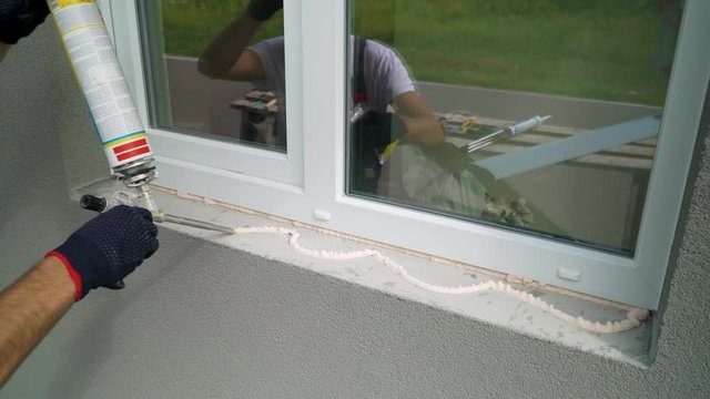 Worker hands in protective gloves applying polyurethane construction foam for window sill installation closeup. Preparation work on building site. Technology, safety policy, building, repair concept