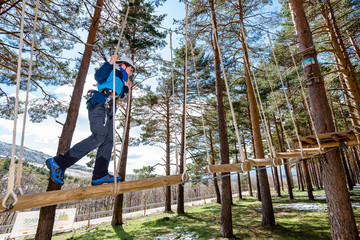Naklejka na ściany i meble A kid evolves through an obstacle hanging from the trees at an adventure park in Segovia, Spain