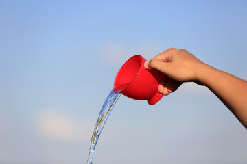 Kobieca dłoń wylewa wodę z czerwonej filiżanki. - obrazy, fototapety, plakaty