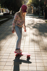 Obraz na płótnie Canvas blond girl with pink skateboarding in park. Teenager girl with penny skateboard on street. Childhood, summer, vacation, sports 