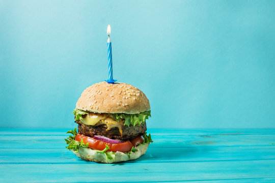 Homemade burger barbeque sandwich with beef and lit candle for birthday party on blue background. Concept holiday