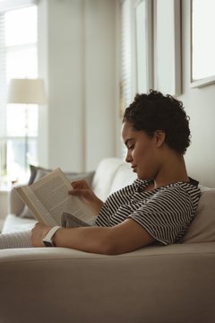 Young woman reading book while sitting on sofa