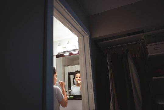 Young woman standing in front of mirror brushing her teeth in