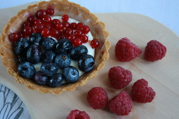 A cookie filled with cream and fruit surrounded by raspberries