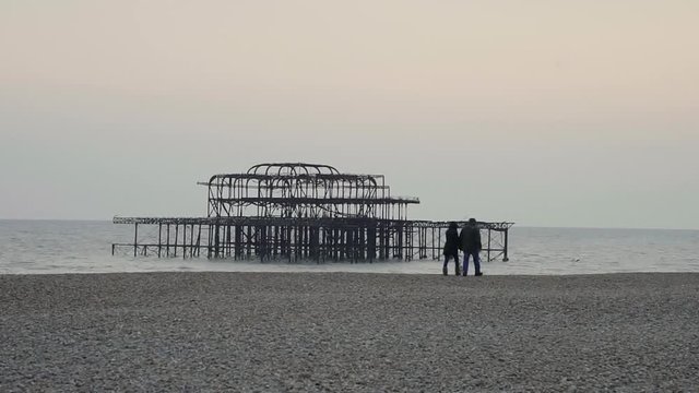 Brighton beach - Burned down west pier - Couple walking by with dog - 50% speed