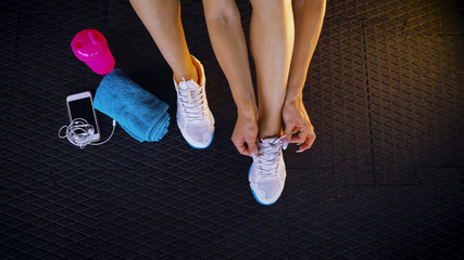 Top view of a fit woman seated on the floor of a gym tying shoelaces sneakers. Healthy lifestyle. Sport and cardio workout concept