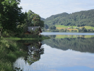 Fototapeta premium SunReflection of house and trees in crystal clear lake water