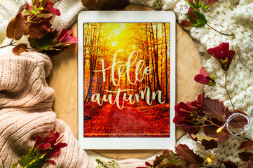 The tablet says the word hello Autumn with red leaves and a dais on the wooden background. Concept...