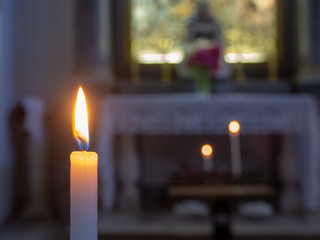 The flame of a candle with the church altar in the background