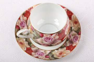 Empty porcelain tea cup with saucer and floral pattern on a table with white tablecloth