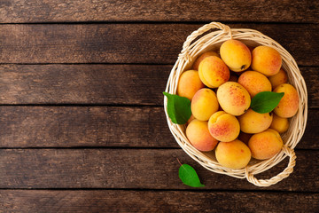 Naklejka na ściany i meble Fresh apricots in wicker basket on dark wooden background