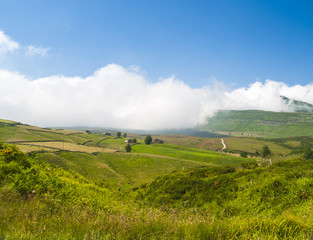 Niebla subiendo por un verde valle contrastando con un cielo azul intenso.