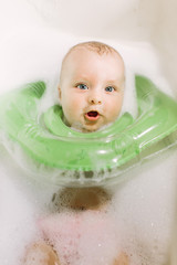 he baby is newborn, the girl is bathing in the bathroom with a inflatable circle around her neck.