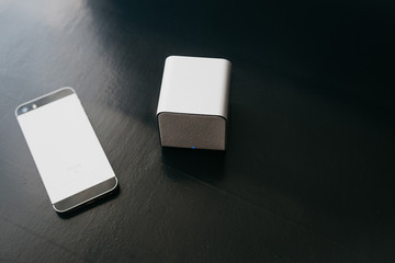 Wireless speakers and a cell phone next to them on a dark background. Modern technology for...