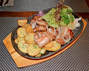 Fried pork with a garnish from potatoes and vegetables on a frying pan