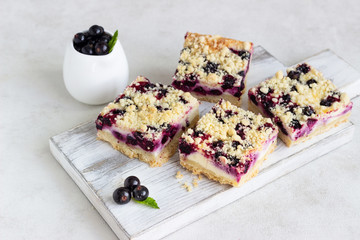 Black currant cake. Cheesecake bars with lemon, black currant and streusel on a white wooden cutting board.